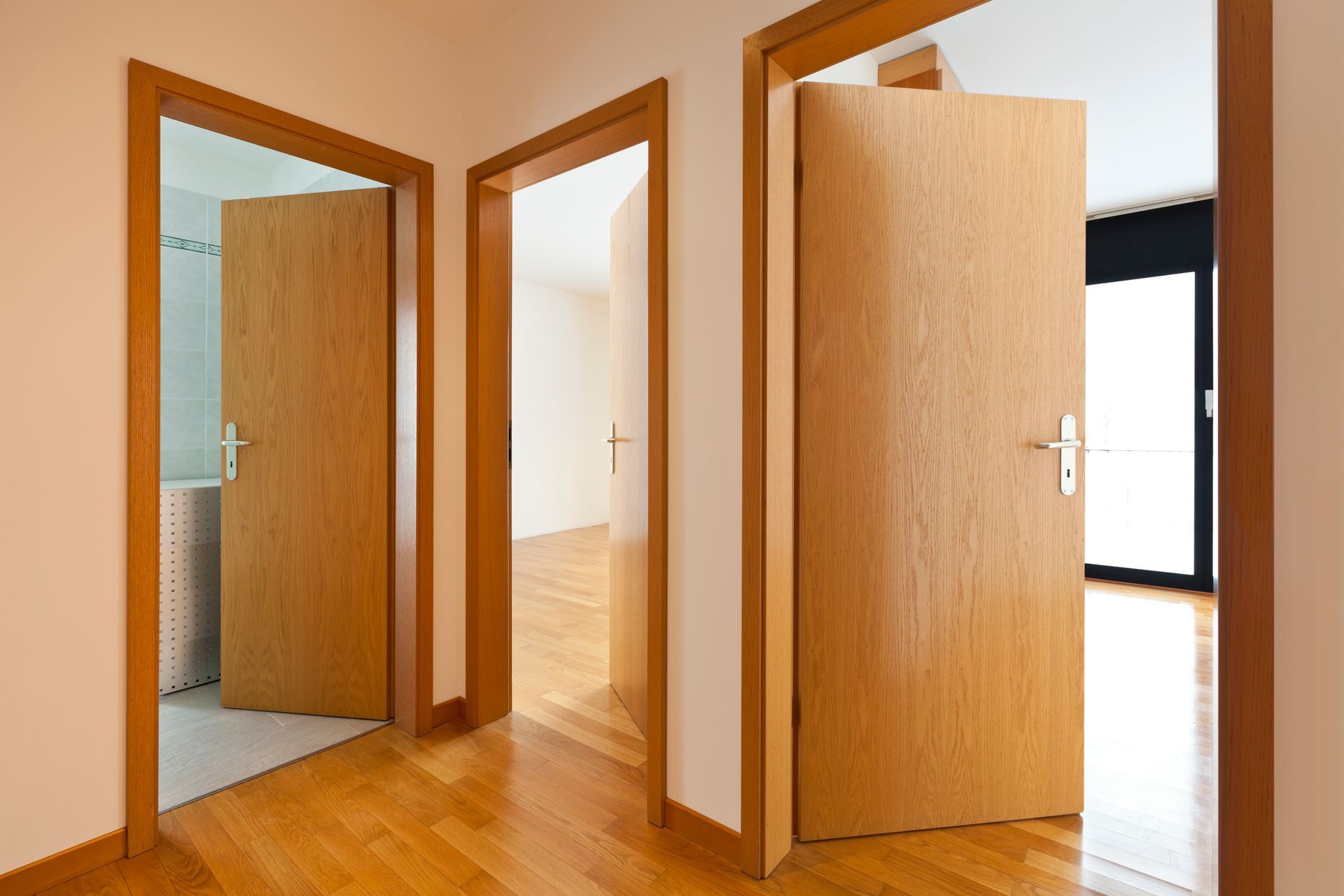 Un couloir avec un parquet clair et trois portes ouvertes aux encadrements assortis en chêne clair.