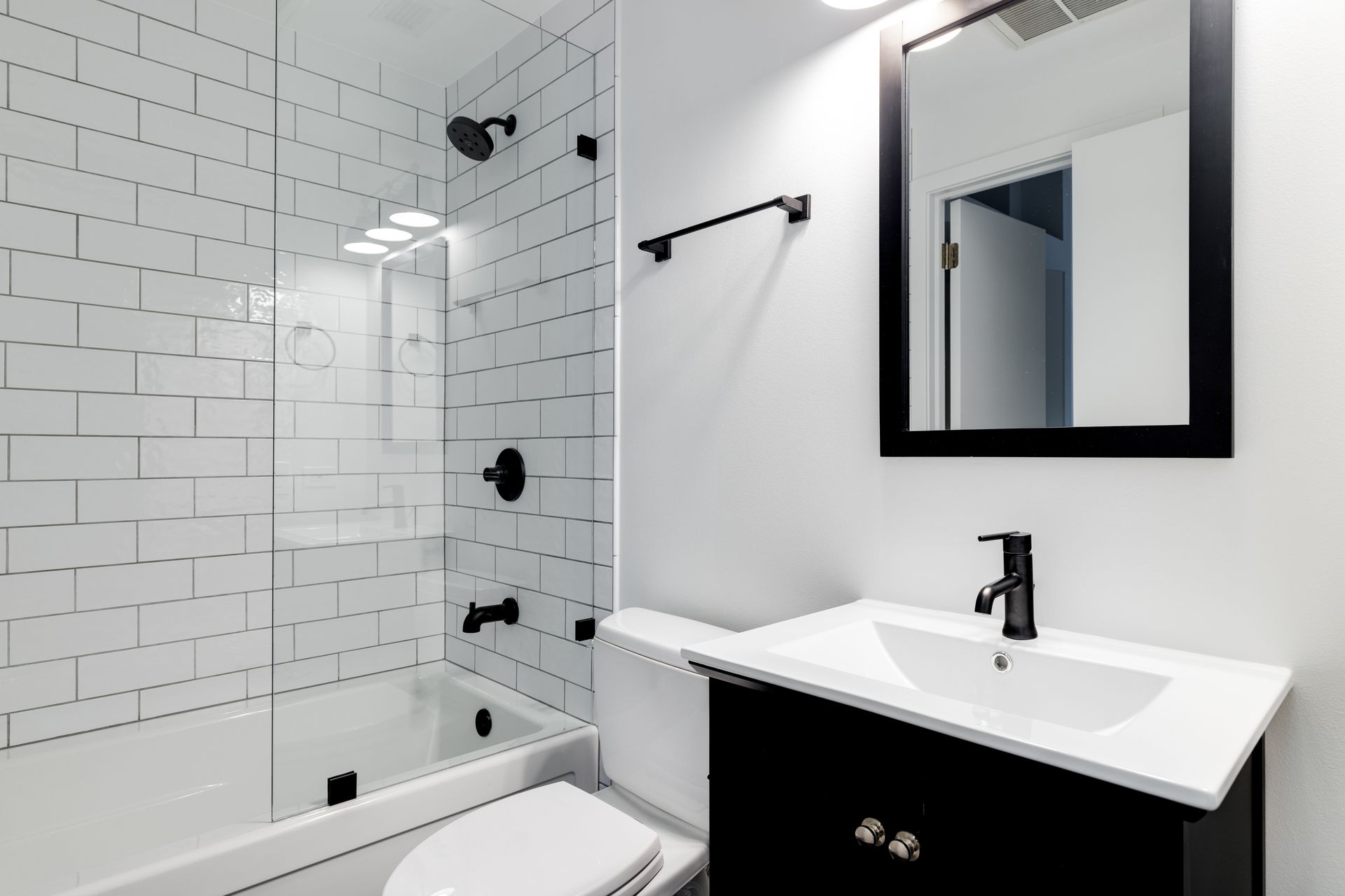 Une salle de bains moderne avec des carreaux de métro blancs, un miroir à cadre noir, un meuble lavabo noir et des accessoires de douche noirs.