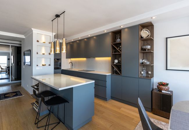 Cuisine moderne avec armoires gris foncé, îlot en quartz avec tabourets de bar, éclairage sous les armoires et parquet.