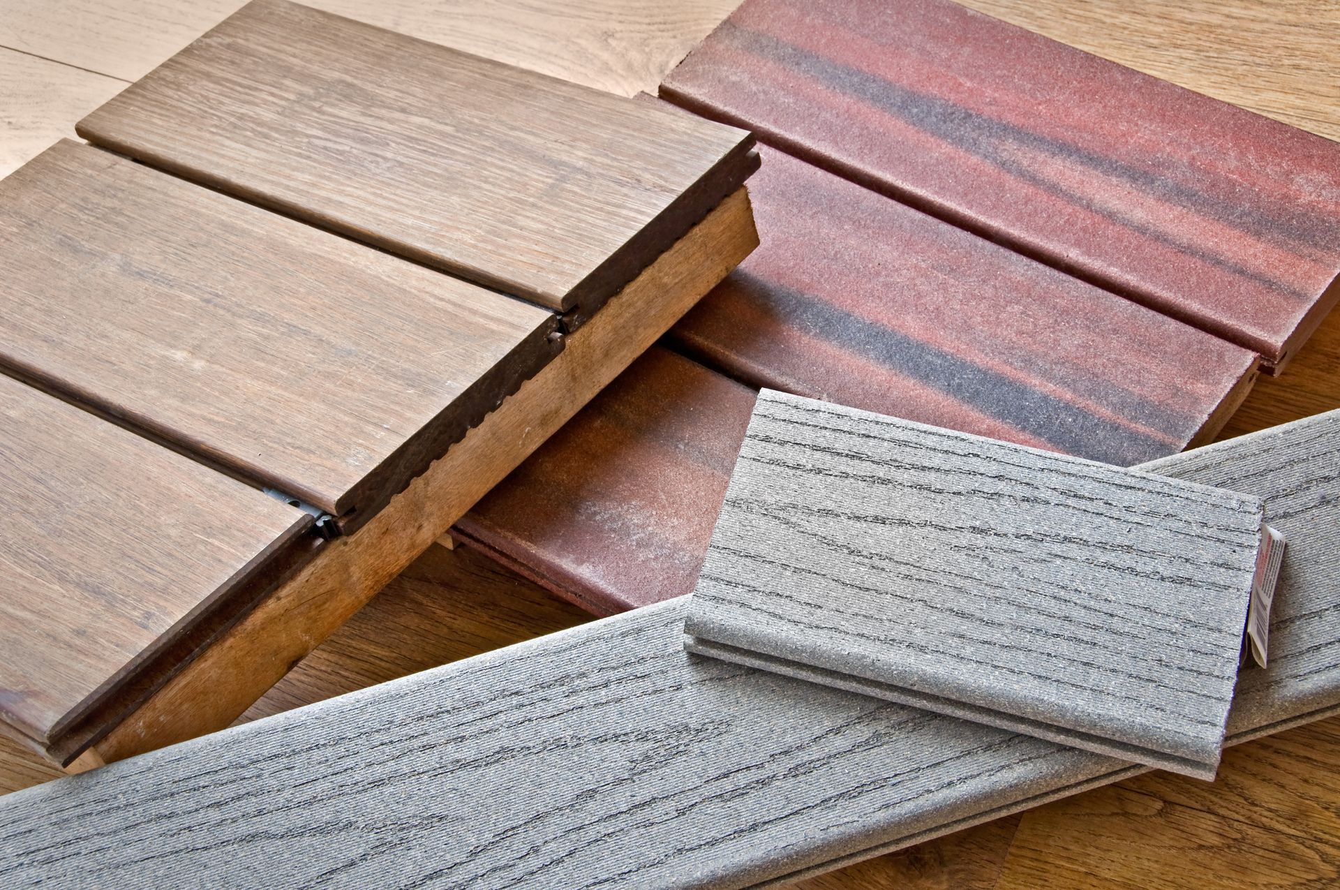 Échantillons de lames de terrasse composites brunes et grises présentant différentes textures de grain de bois, disposés sur une surface.