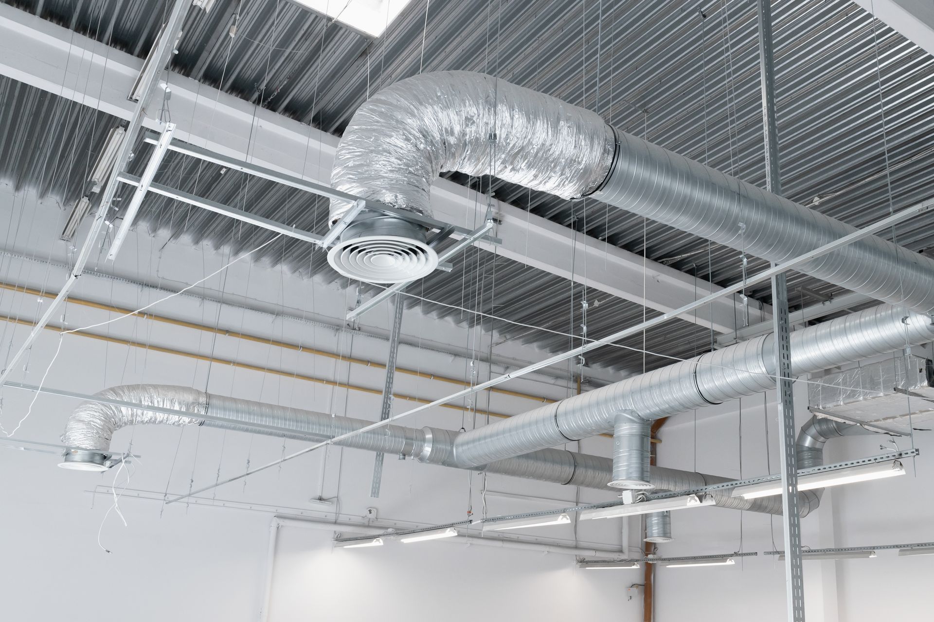 Conduits de ventilation CVC métalliques et luminaires de plafond installés contre un toit ondulé de style industriel.