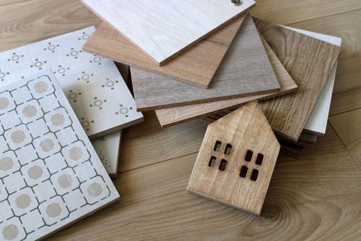 Une collection d'échantillons de bois et de carreaux à motifs disposés sur une surface en bois avec une petite décoration en bois en forme de maison.