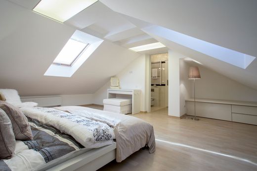 Une chambre mansardée lumineuse et minimaliste avec un lit, un petit bureau, un tabouret de coiffeuse et un lampadaire sous un plafond en pente.