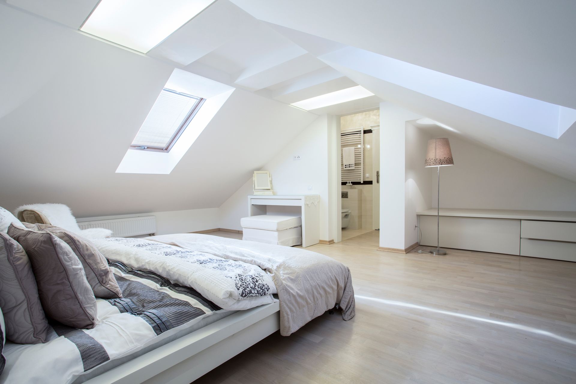 Une chambre mansardée lumineuse et moderne, avec un lit paré de draps à motifs, un bureau, un lampadaire et un intérieur minimaliste.