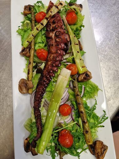 Un plato blanco cubierto con verduras y un pulpo sobre una mesa.