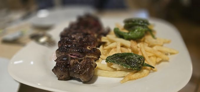 Un plato blanco cubierto con carne y papas fritas sobre una mesa.