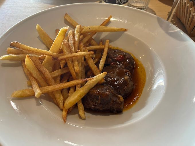 Un plato blanco cubierto con carne y papas fritas sobre una mesa.