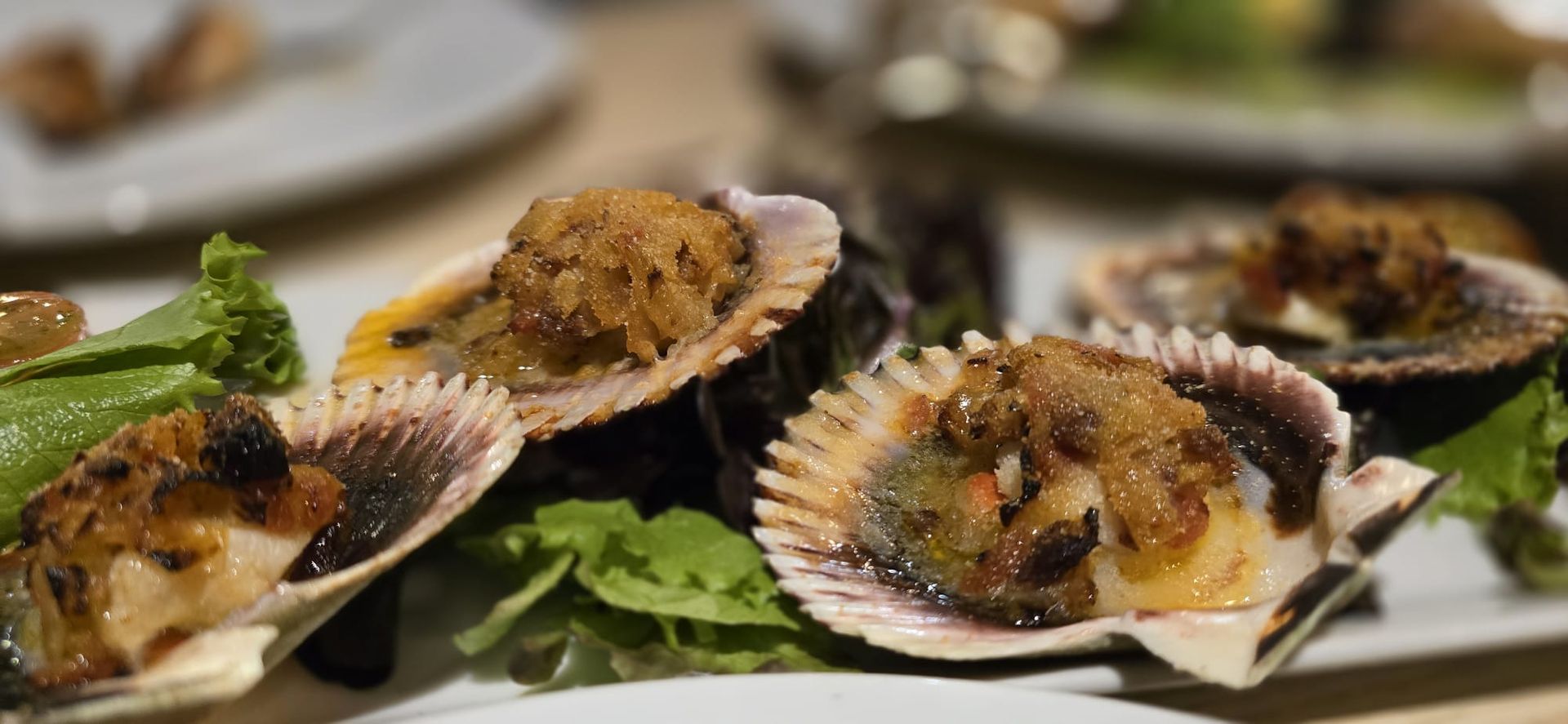 Un plato blanco cubierto con ostras y lechuga sobre una mesa.