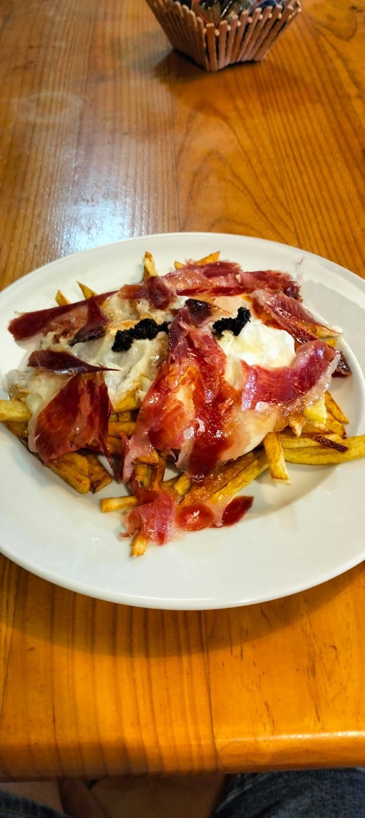 Un plato blanco con carne y papas fritas sobre una mesa de madera.