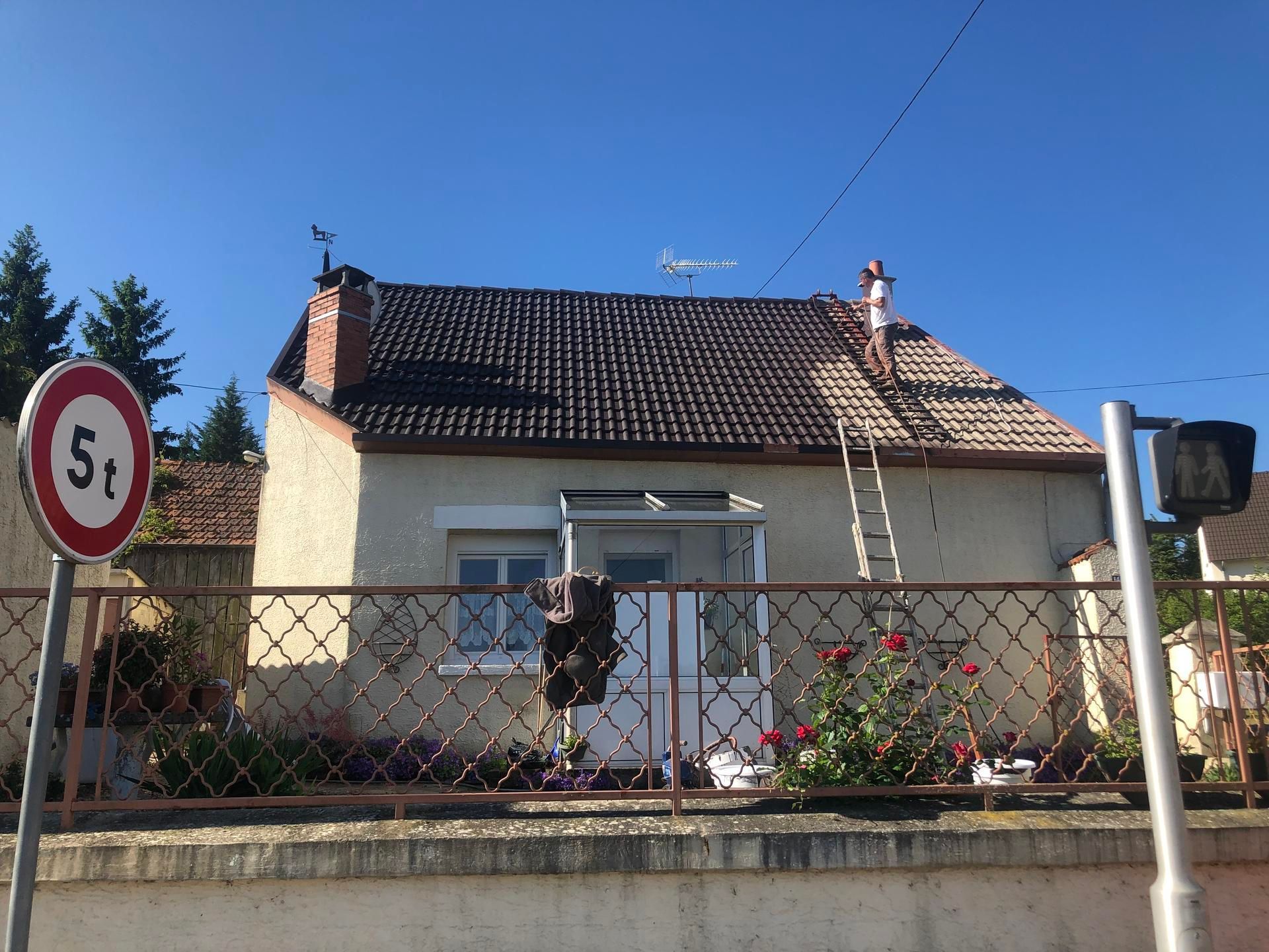 Petite maison avec un toit de tuiles brunes, une échelle et un panneau de limite de poids.