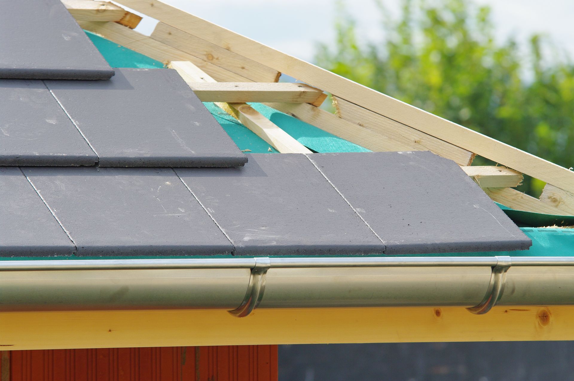Pose de tuiles sur une charpente de toit en bois, avec gouttière au premier plan.