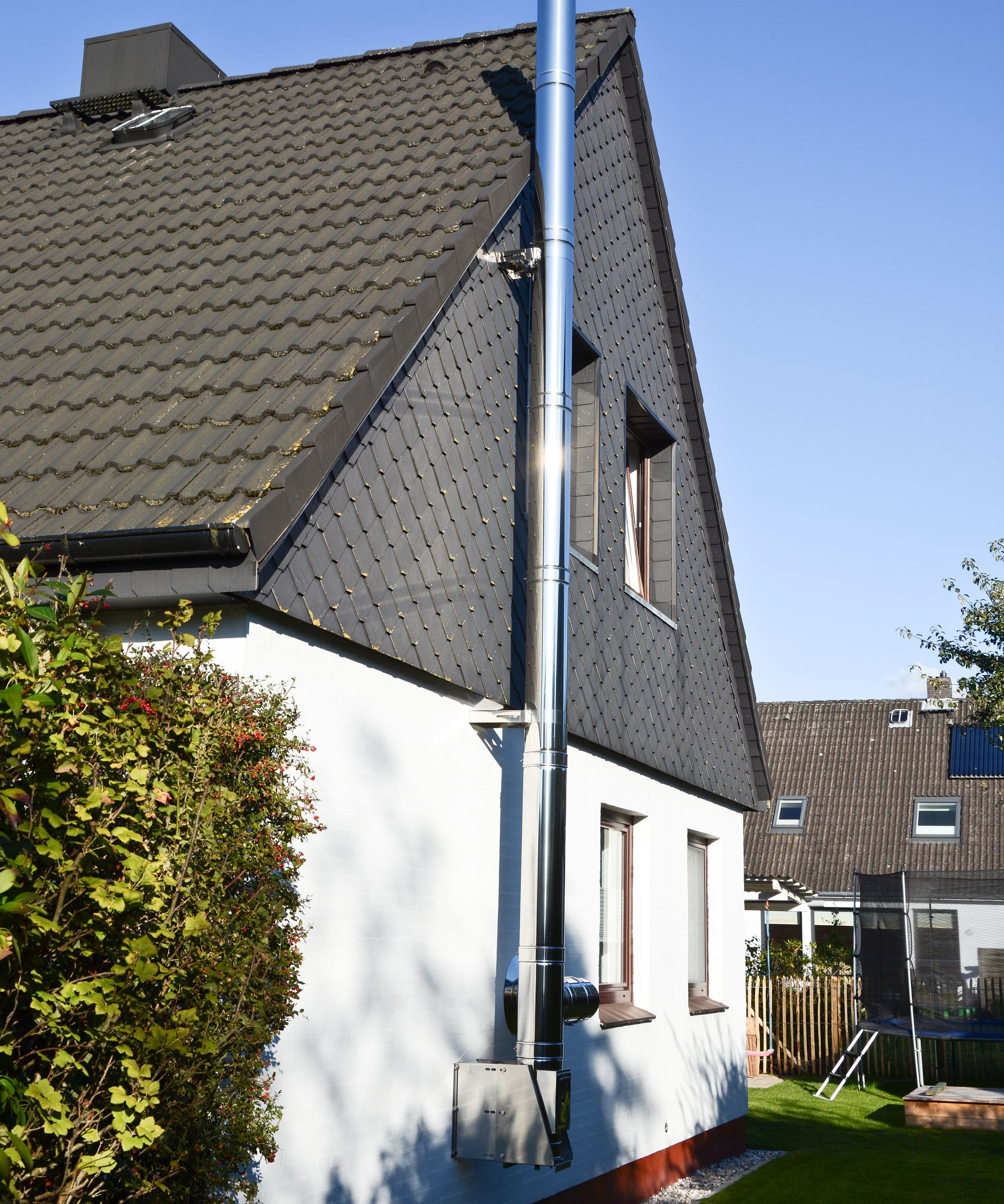 Vue extérieure d'une maison avec une haute cheminée métallique sur un toit de bardeaux gris, par une journée ensoleillée.