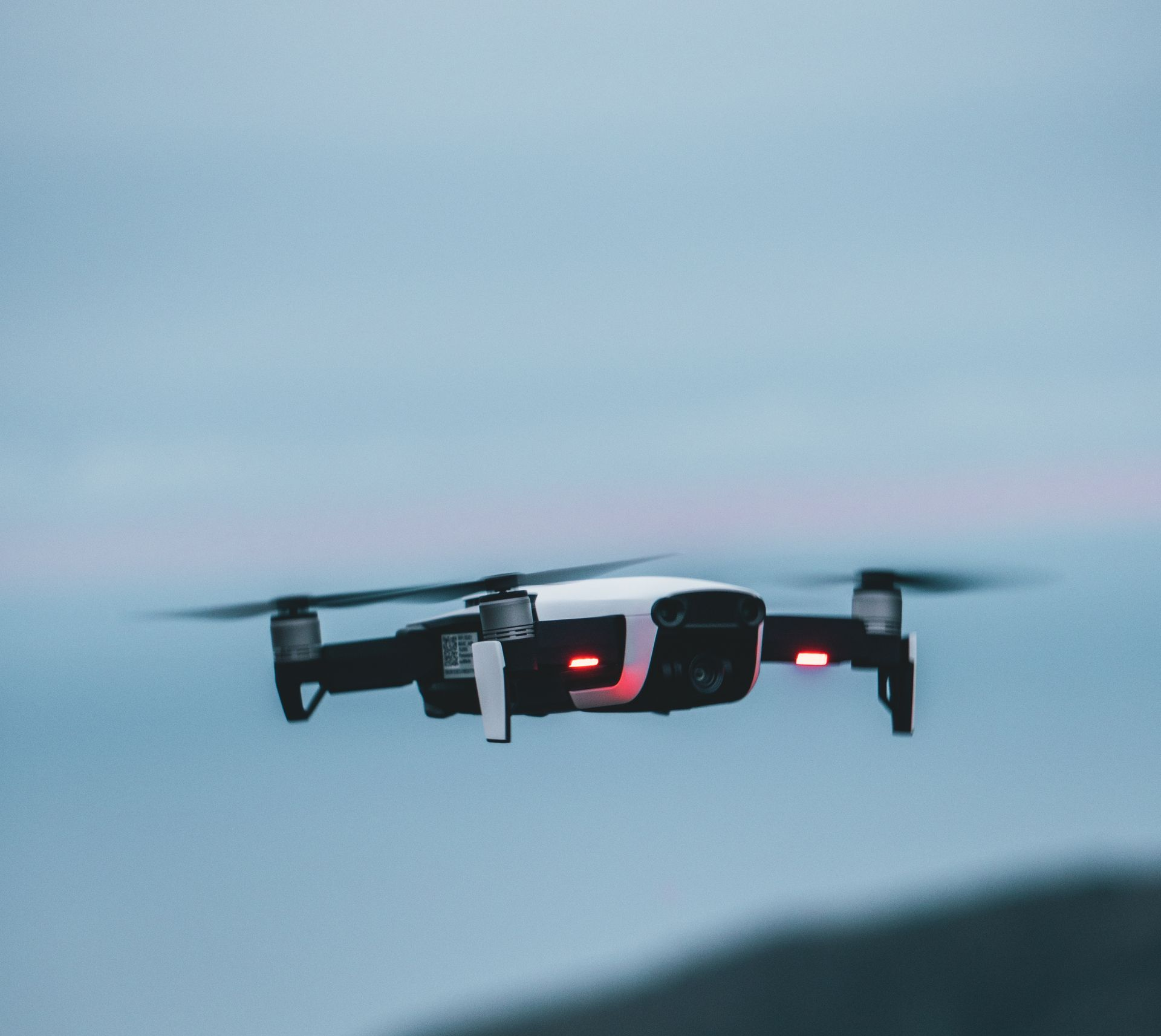 Drone en vol sur fond de ciel bleu, lumières rouges allumées.