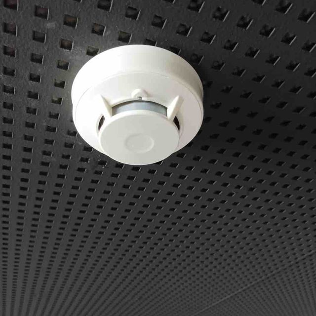 Un detector de humo blanco está montado en un techo negro.