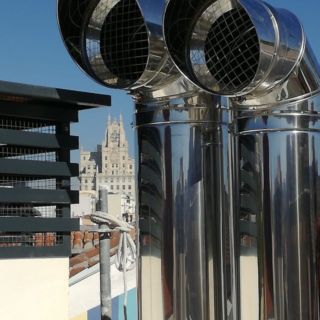 Una hilera de tubos de acero inoxidable con una torre de reloj al fondo