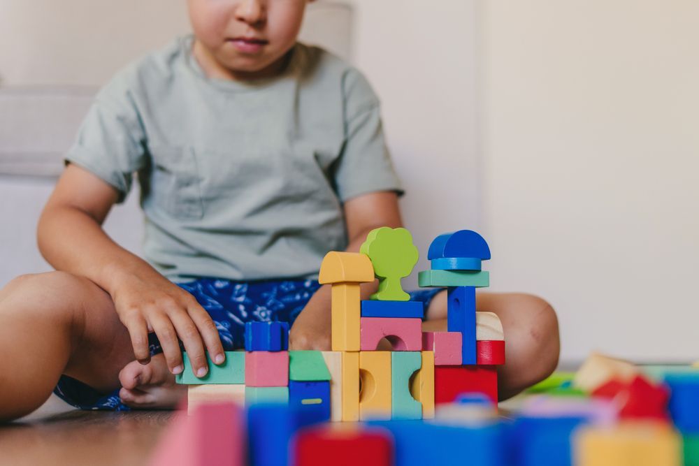 Un niño pequeño está sentado en el suelo jugando con bloques de madera.