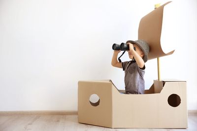 Un niño pequeño está sentado en un bote de cartón mirando a través de binoculares.
