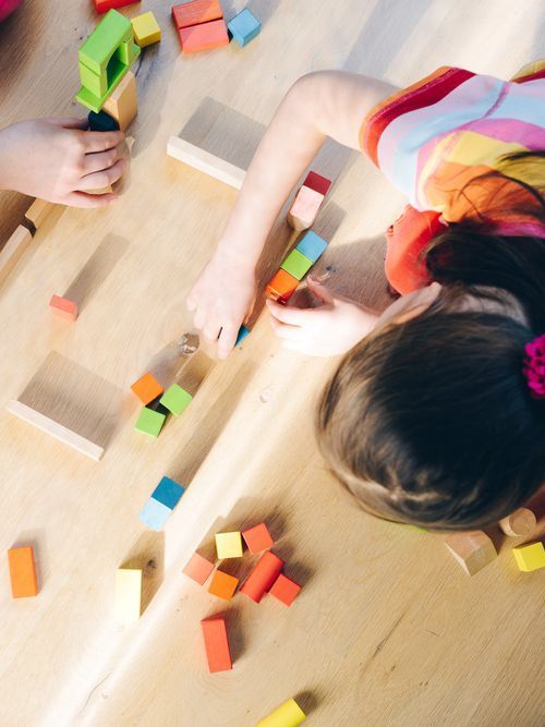 Una niña está jugando con bloques de madera en una mesa de madera.