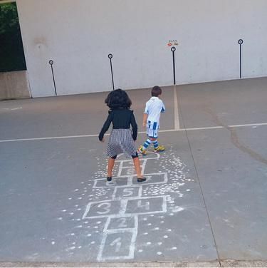 Dos niños están jugando a la rayuela en una cancha de concreto.