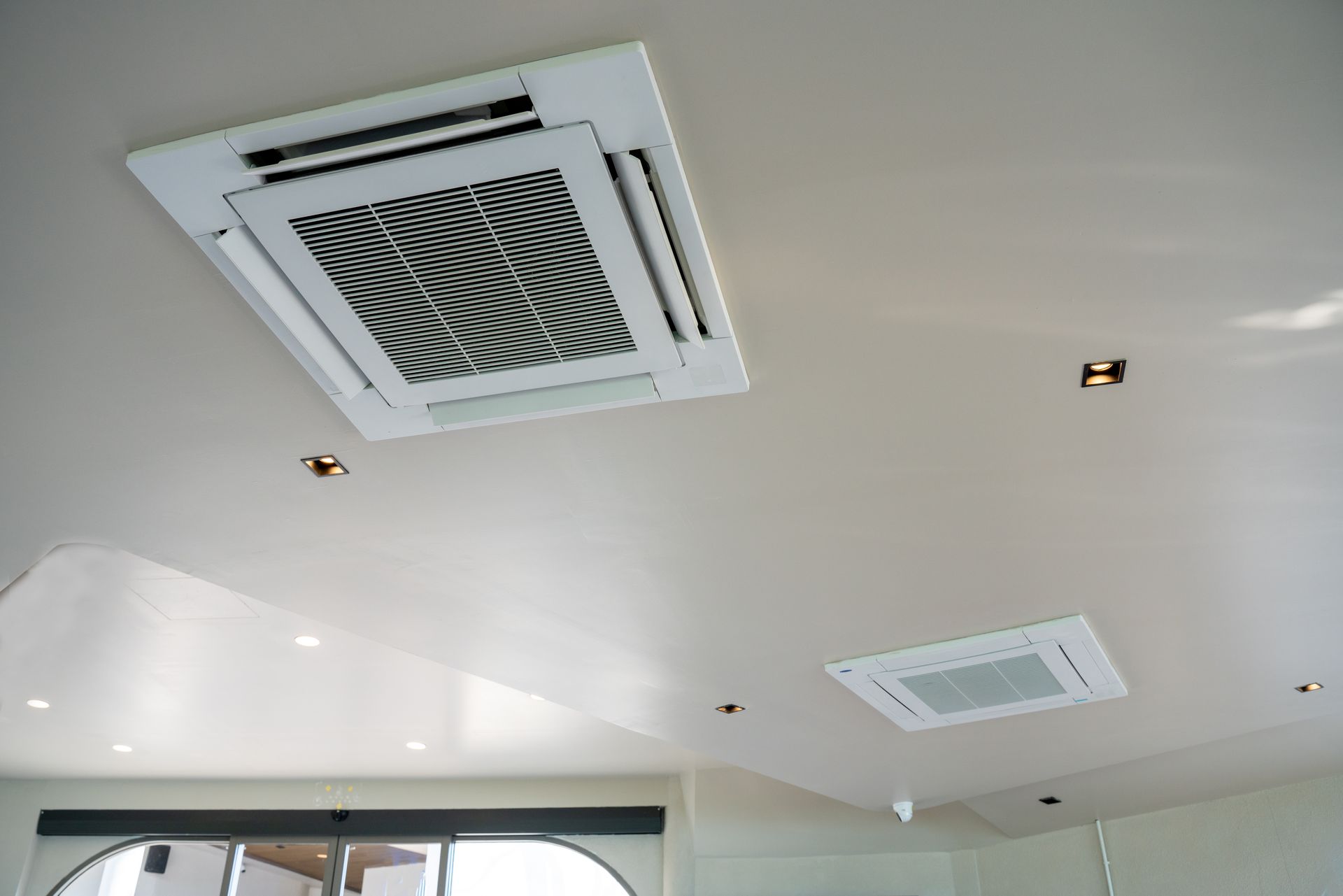 Plafond blanc avec deux bouches d'aération carrées et des spots encastrés dans un intérieur moderne.