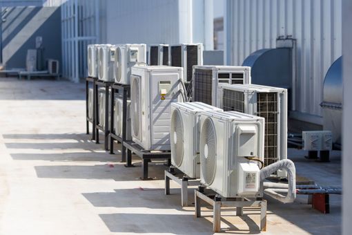 Rangée extérieure d'unités de climatisation sur supports métalliques à côté d'un bâtiment industriel gris.
