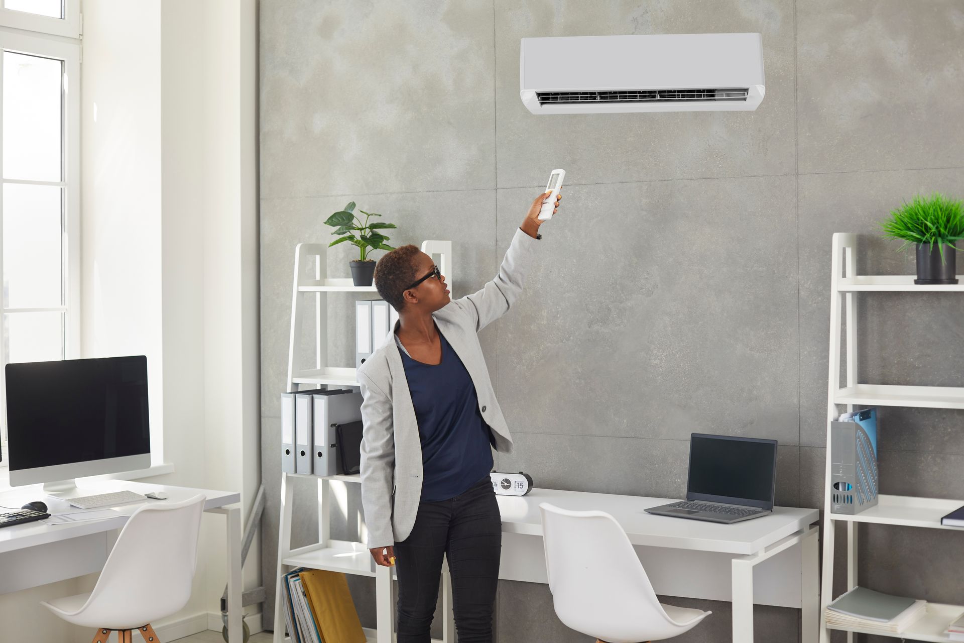 Une personne pointe une télécommande vers un climatiseur mural dans un bureau lumineux.