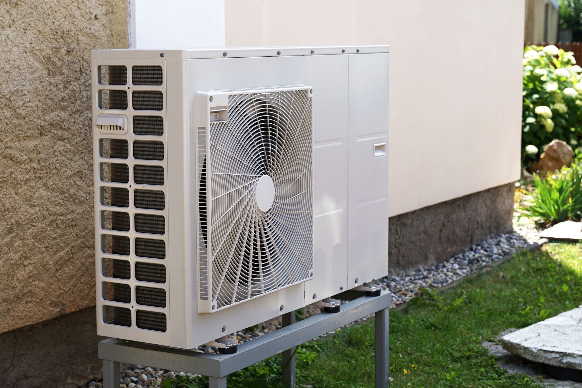 Unité de climatisation extérieure fixée au mur, avec ventilateur et panneaux de ventilation sur un support métallique.
