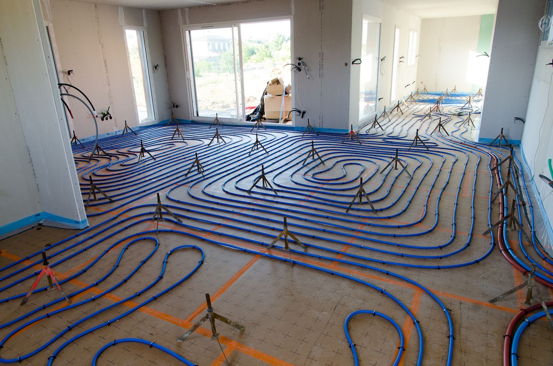 Des tubes de chauffage au sol rayonnants sont installés dans une pièce en construction, dont les murs et les fenêtres ne sont pas finis.