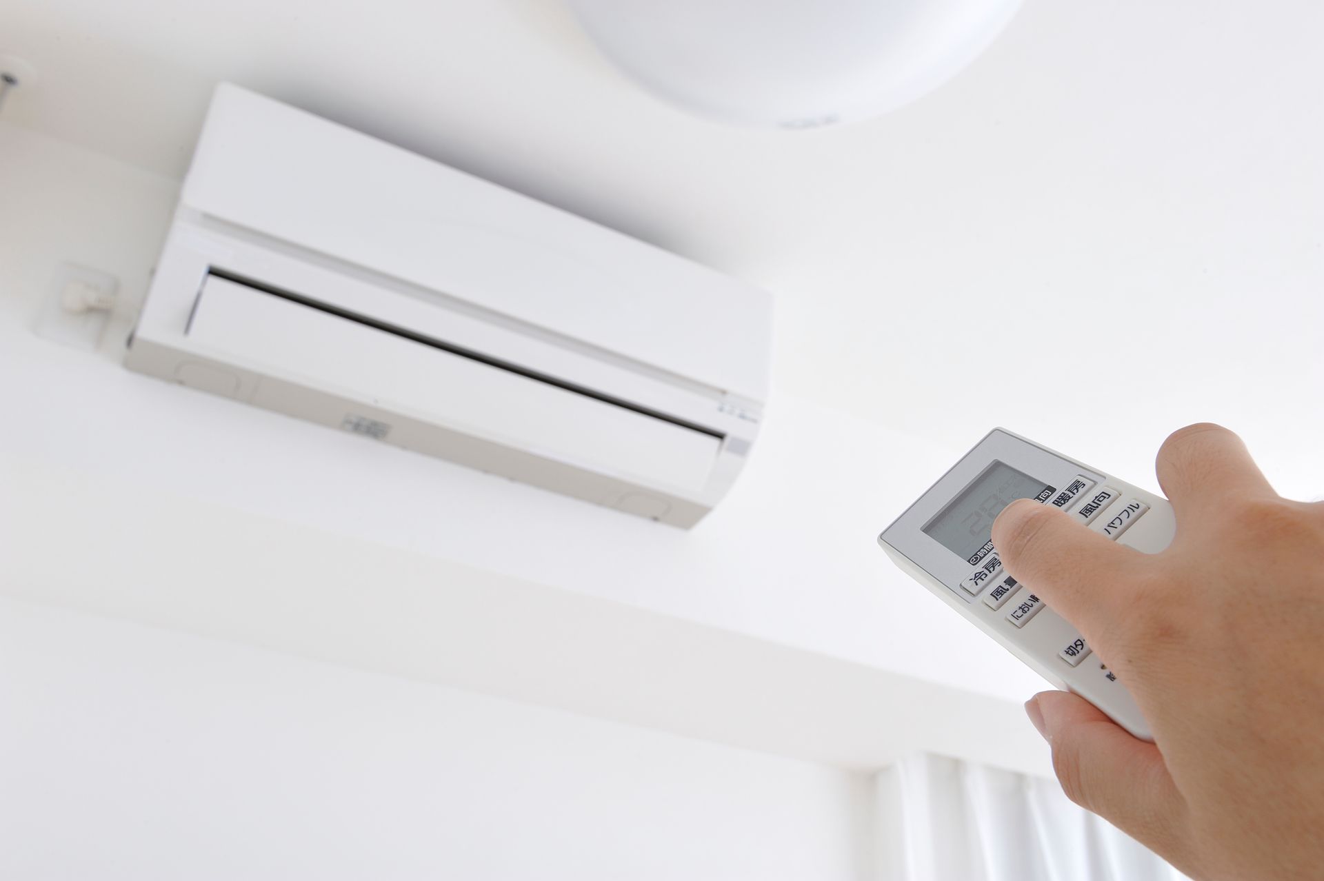 Une main tenant une télécommande pointée vers un climatiseur mural blanc près du plafond.