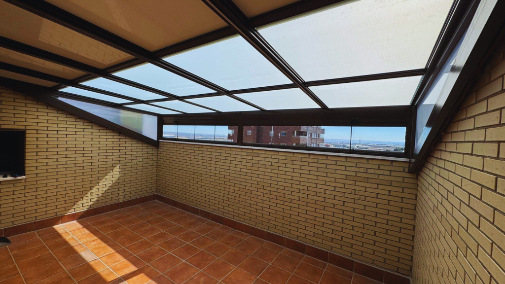 Patio cubierto de ladrillo con baldosas de terracota y techo de vidrio translúcido, con vistas a los edificios cercanos.