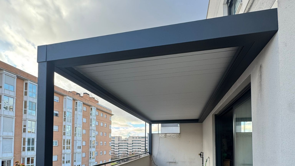 Balcón con toldo oscuro con vistas a edificios de apartamentos bajo un cielo nublado.