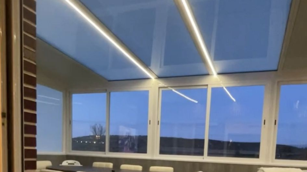 Habitación moderna con grandes ventanales al anochecer y largas lámparas de techo que se reflejan en el cristal.