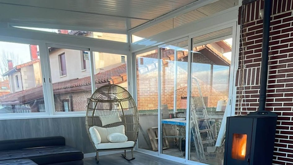 Terraza acristalada con sillón de mimbre con forma de huevo, sofá oscuro, puertas correderas de cristal 