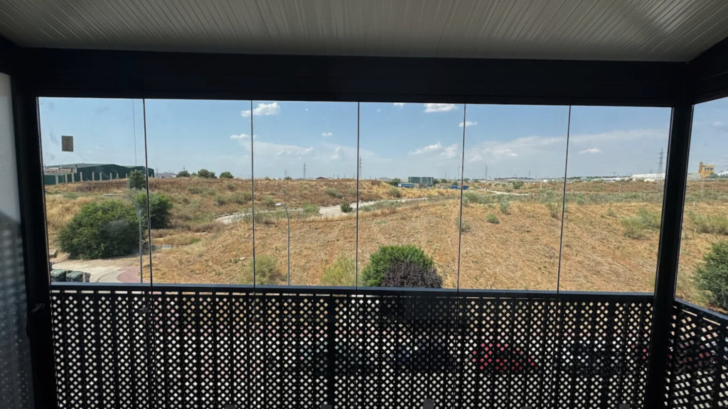 Vista desde un balcón sombreado con vistas a un paisaje árido y rocoso bajo un cielo azul.