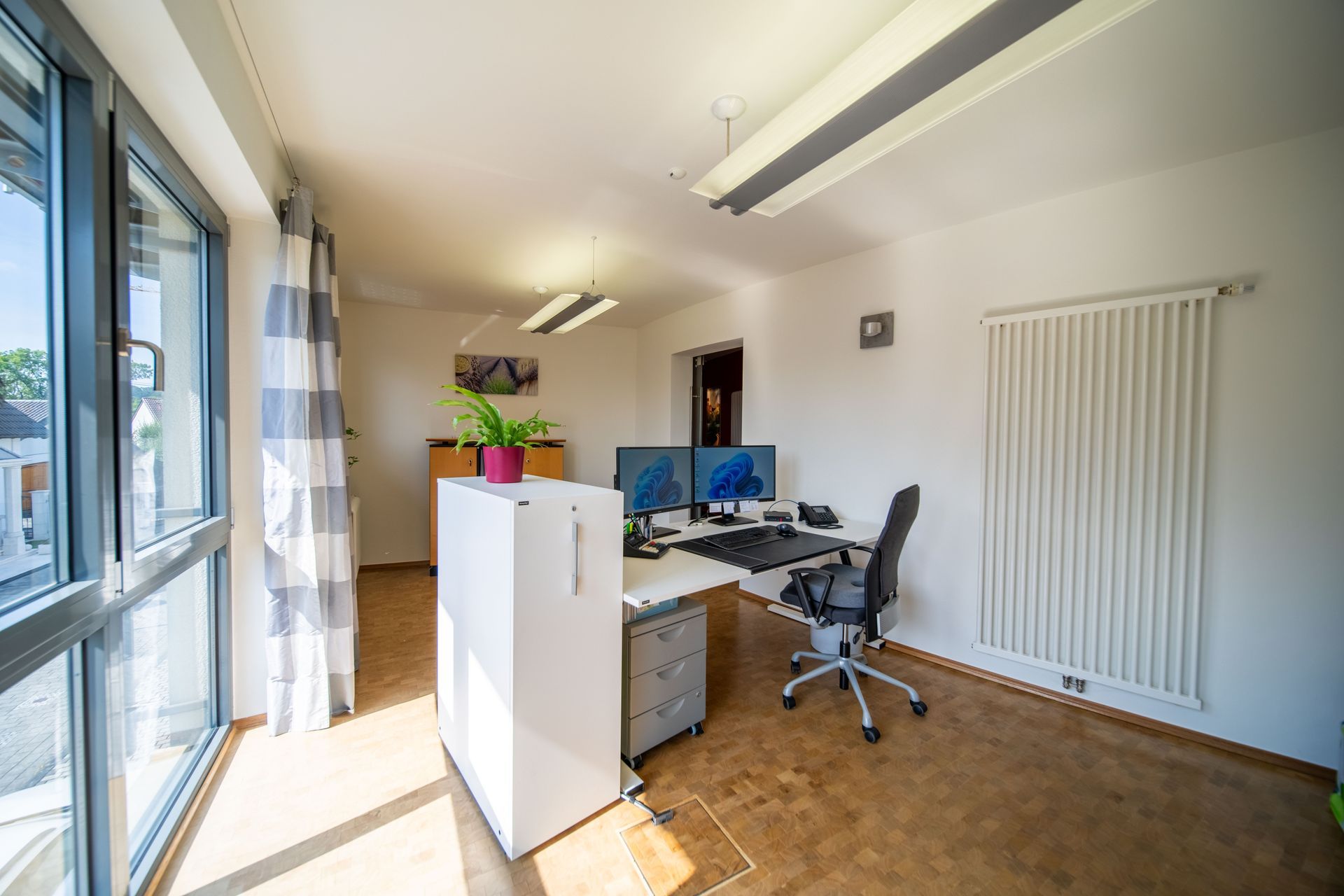 Heller Büroarbeitsplatz mit Schreibtisch, Monitor und Fensterfront.
