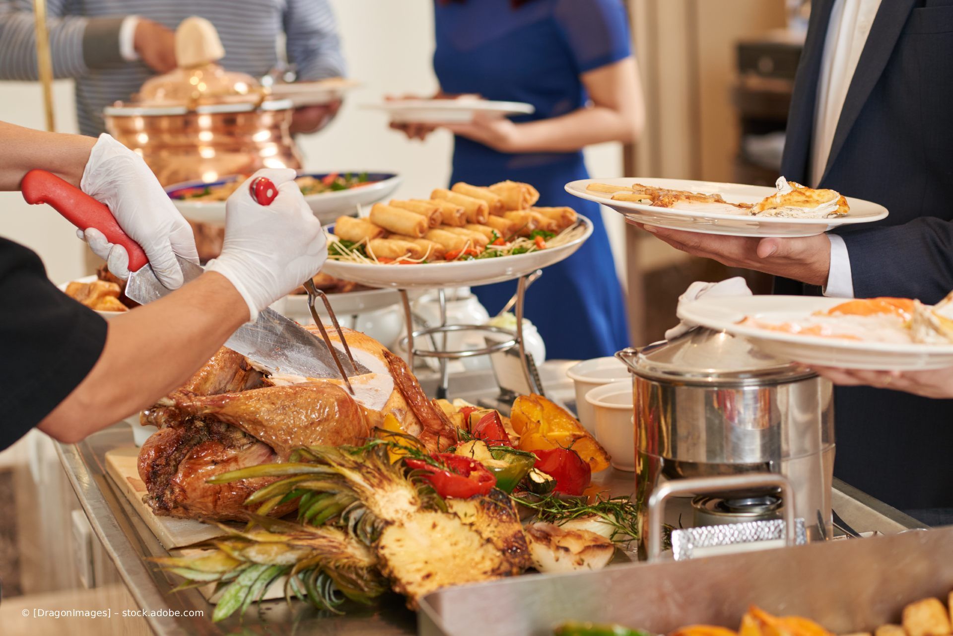 Buffet mit verschiedenen Gerichten, die von einem Koch an Gäste mit Tellern serviert werden.