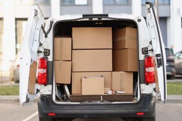 Una camioneta de reparto blanca llena de cajas está estacionada en un estacionamiento.