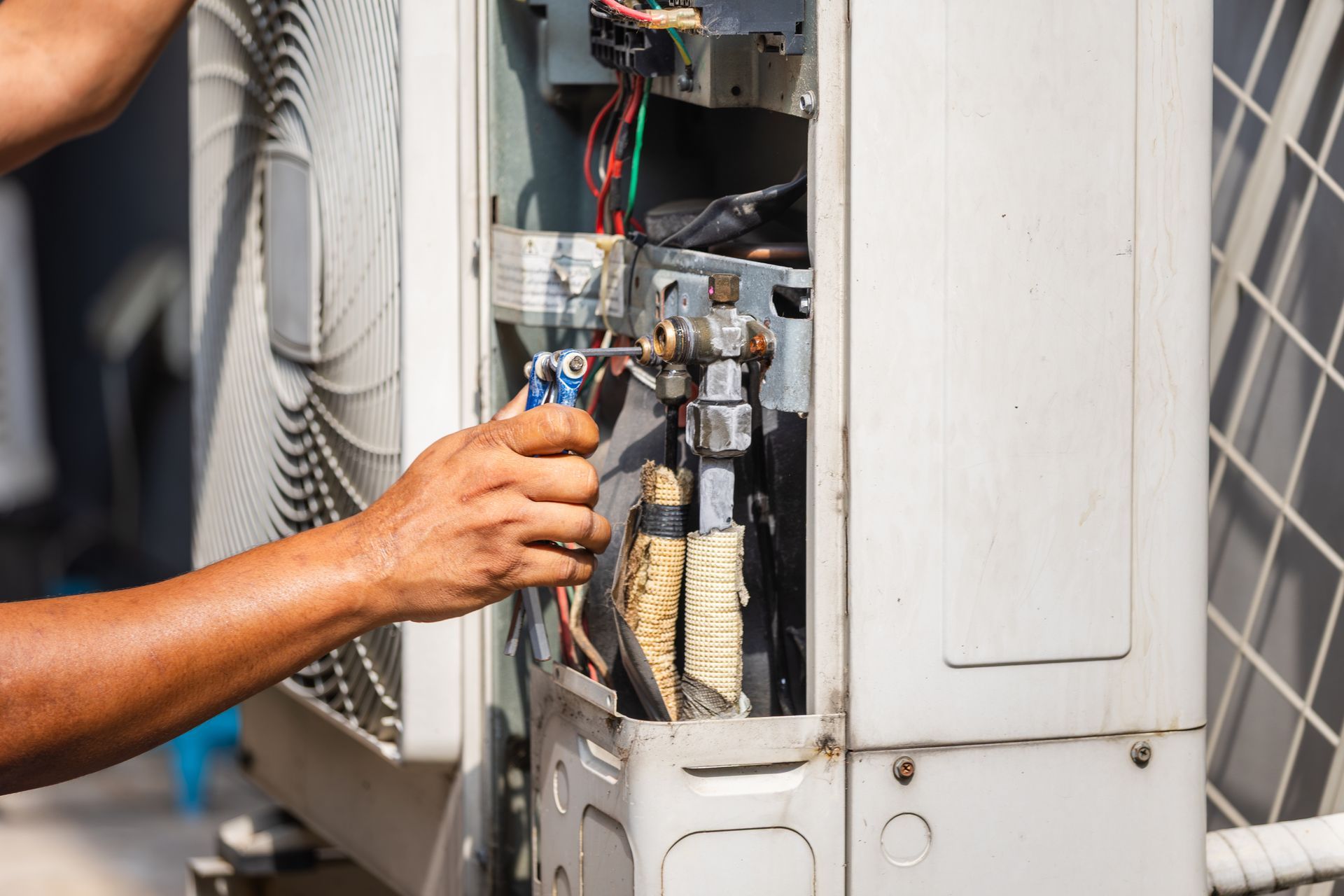 Un technicien inspecte un panneau électrique ouvert sur une unité de climatisation extérieure.