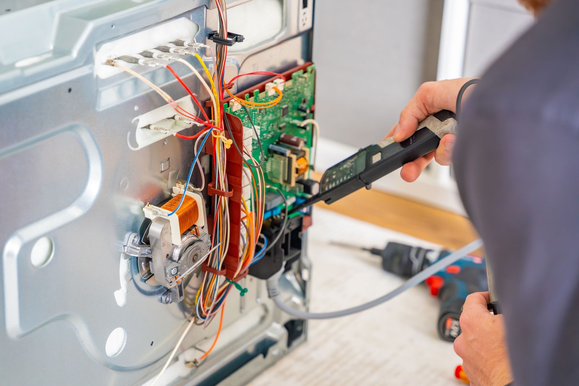 Un technicien utilise un multimètre pour inspecter le câblage à l'intérieur d'un appareil ouvert.