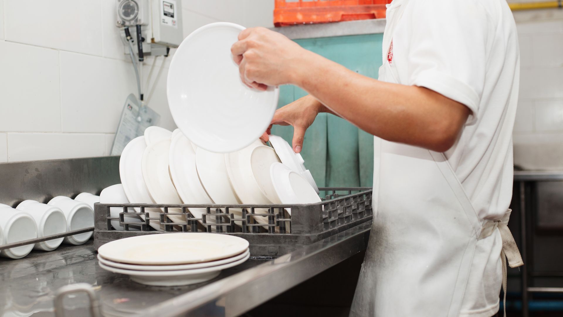 Employé empilant des assiettes blanches dans un égouttoir à vaisselle d'une cuisine professionnelle
