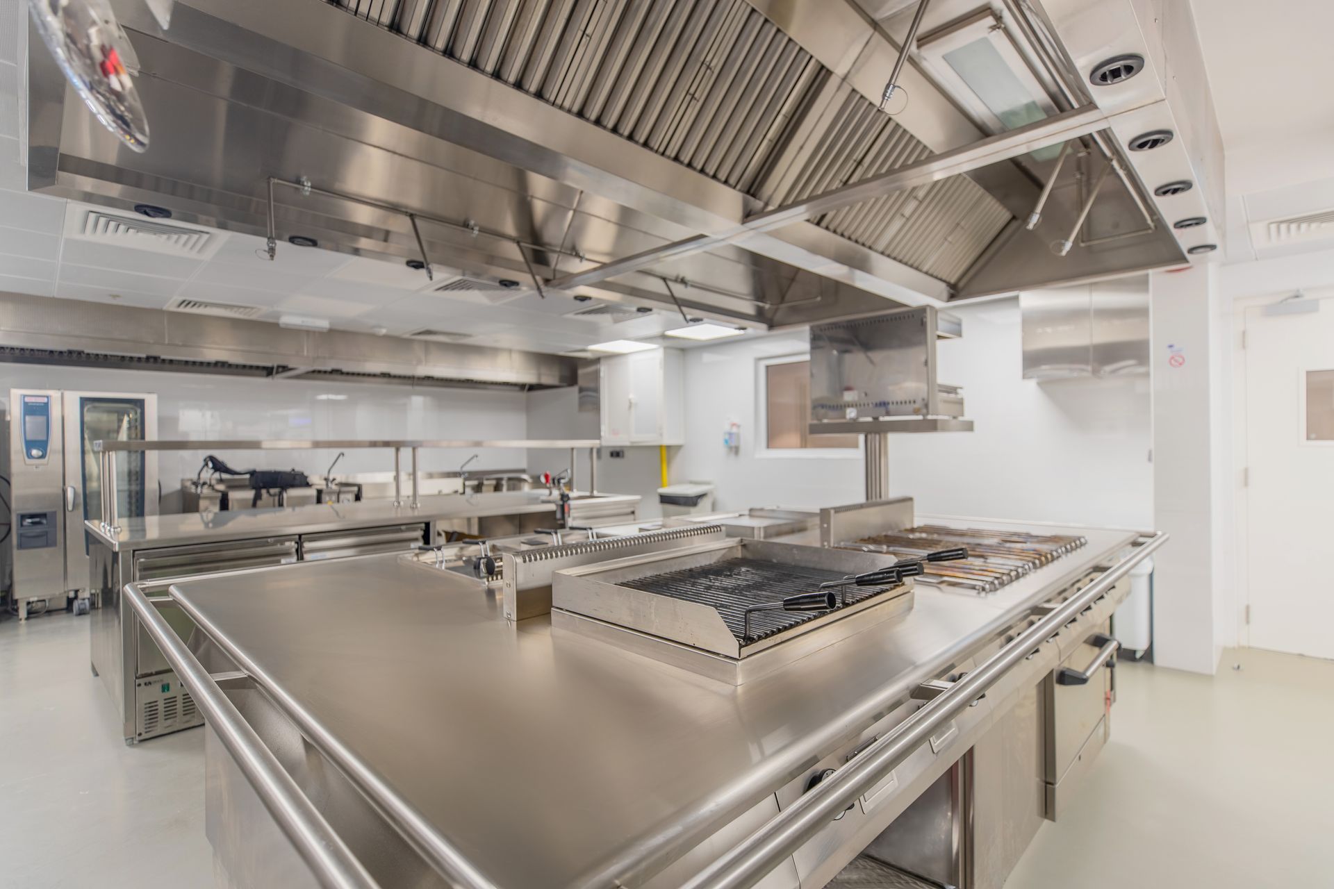 Cuisine commerciale moderne avec comptoirs en acier inoxydable, plaque de cuisson et hotte aspirante.