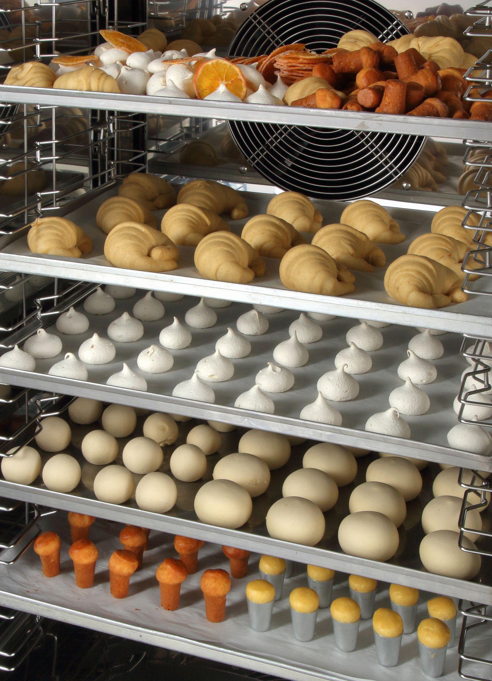 Des rangées de pâtisseries assorties refroidissent sur des grilles métalliques de boulangerie.