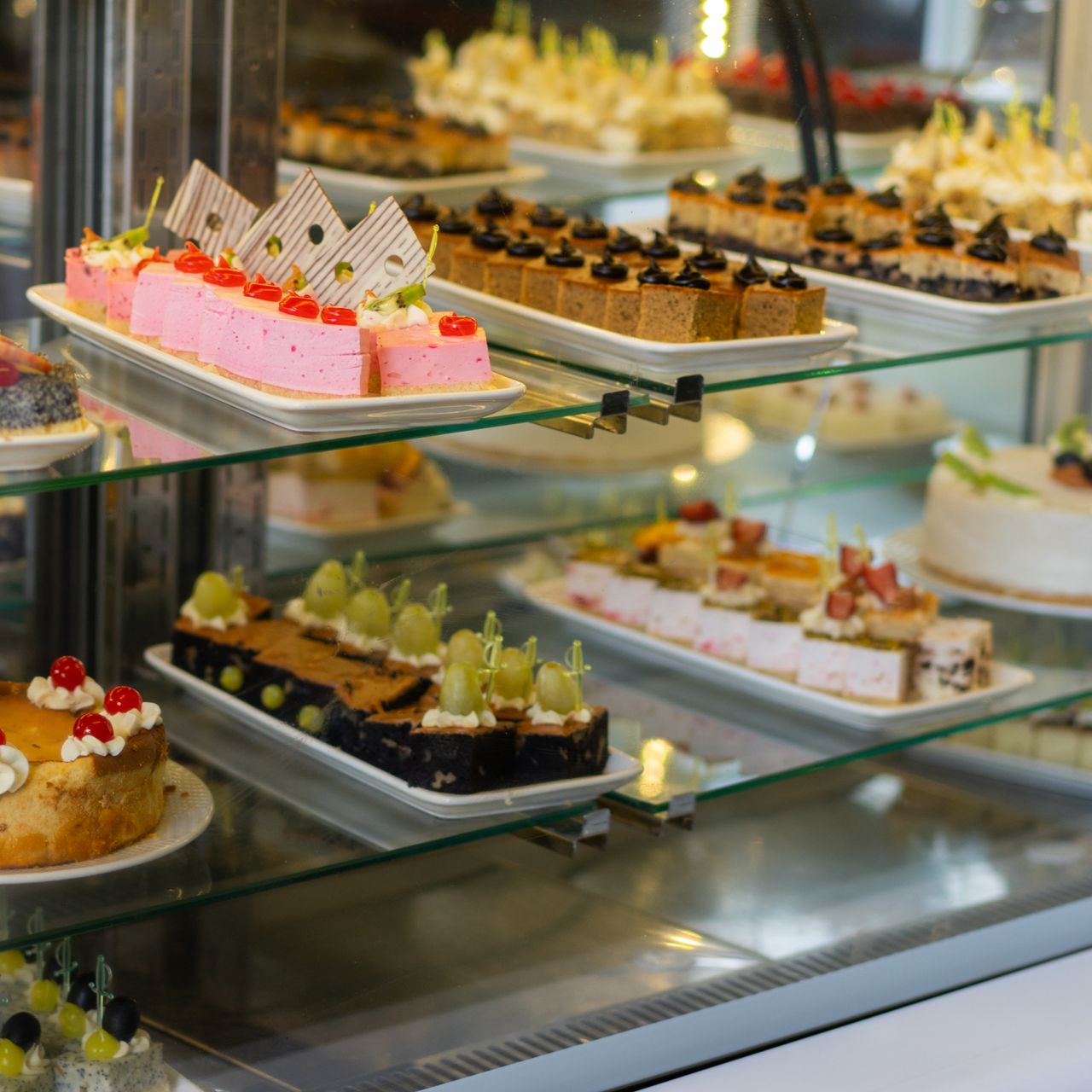 Assortiment de pâtisseries et gâteaux aux teintes pastel présentés sur des étagères en verre dans une vitrine de boulangerie.