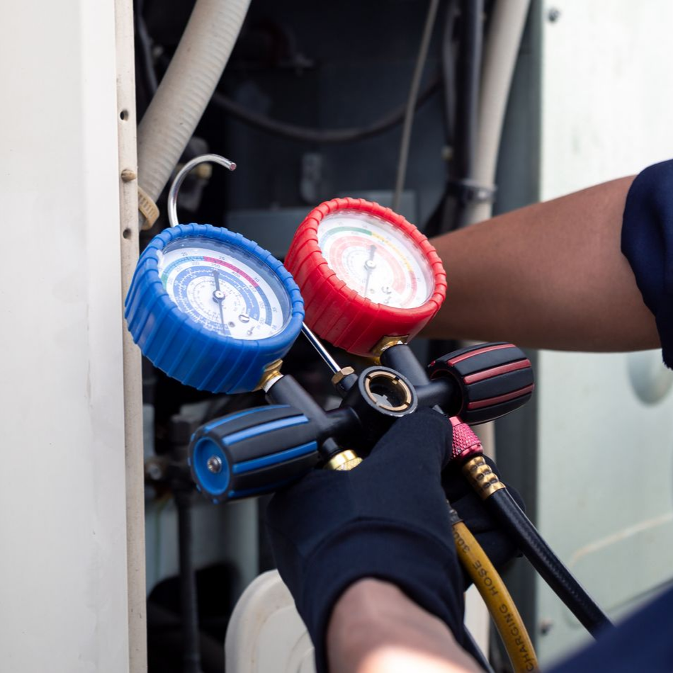 Technicien utilisant des manomètres à collecteur pour l'entretien d'un équipement de CVC, avec des cadrans bleus et rouges et des tuyaux raccordés