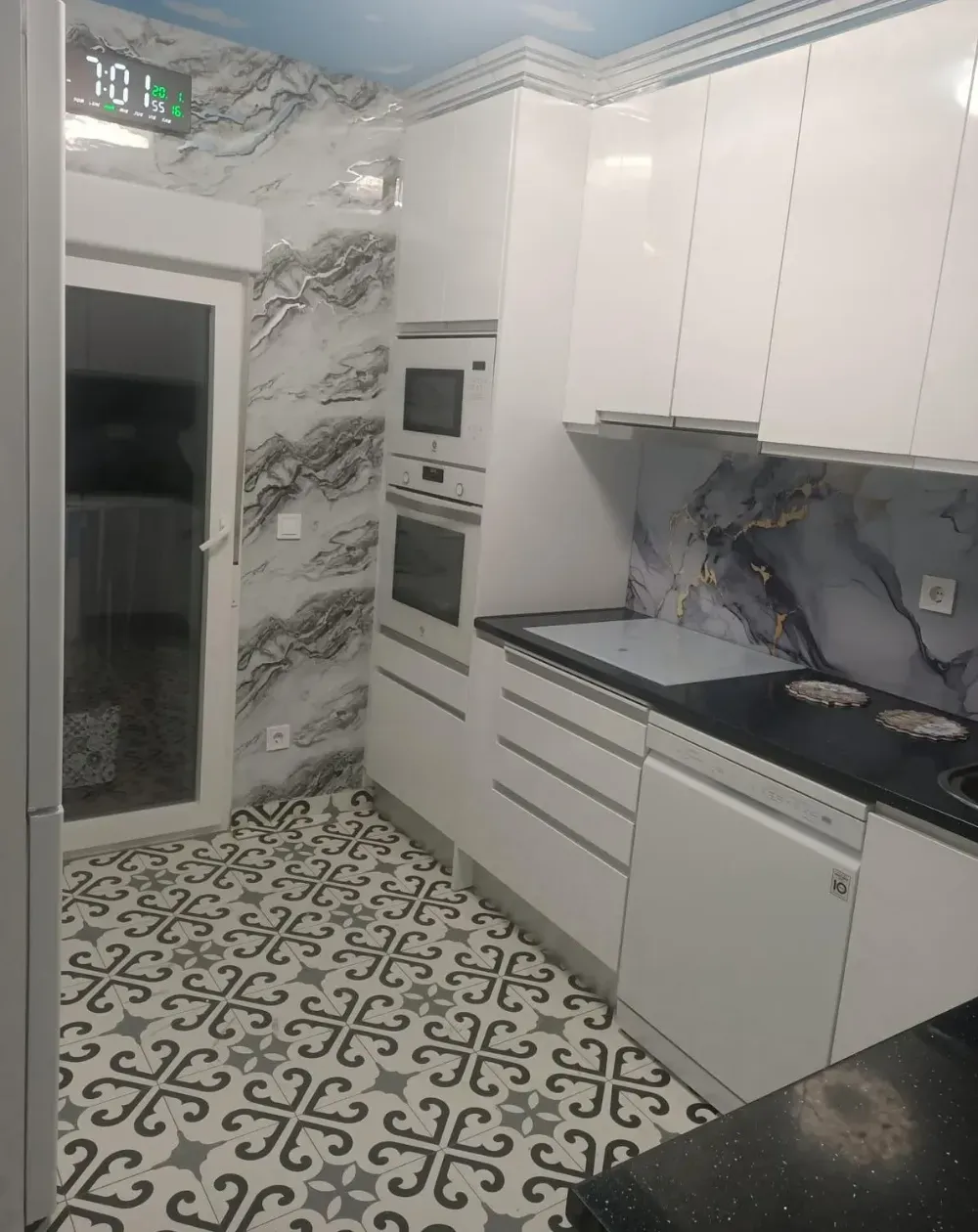 Cocina moderna blanca con paredes que imitan el mármol, encimeras negras y baldosas estampadas en el suelo.