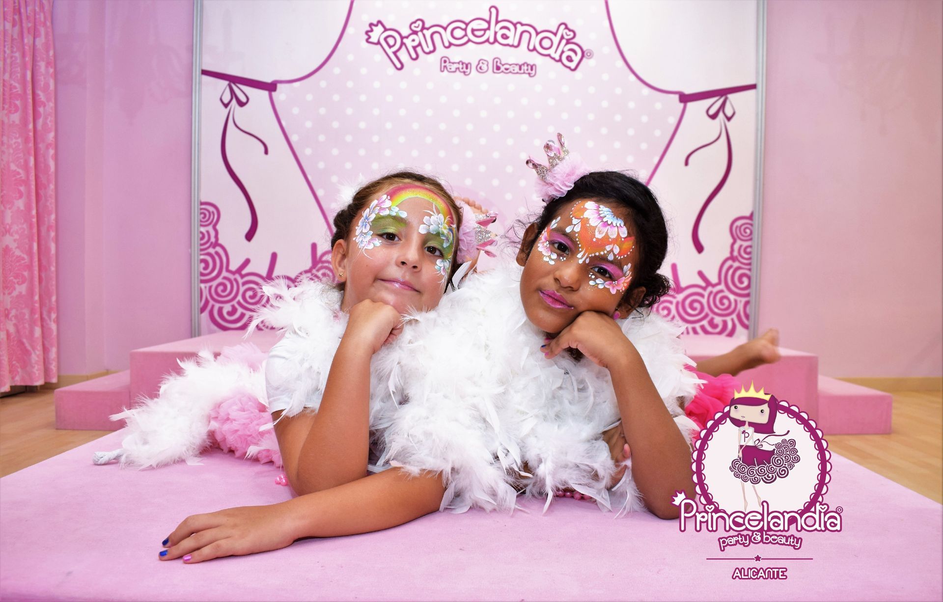 Dos niñas con la cara pintada están recostadas sobre una alfombra rosa.