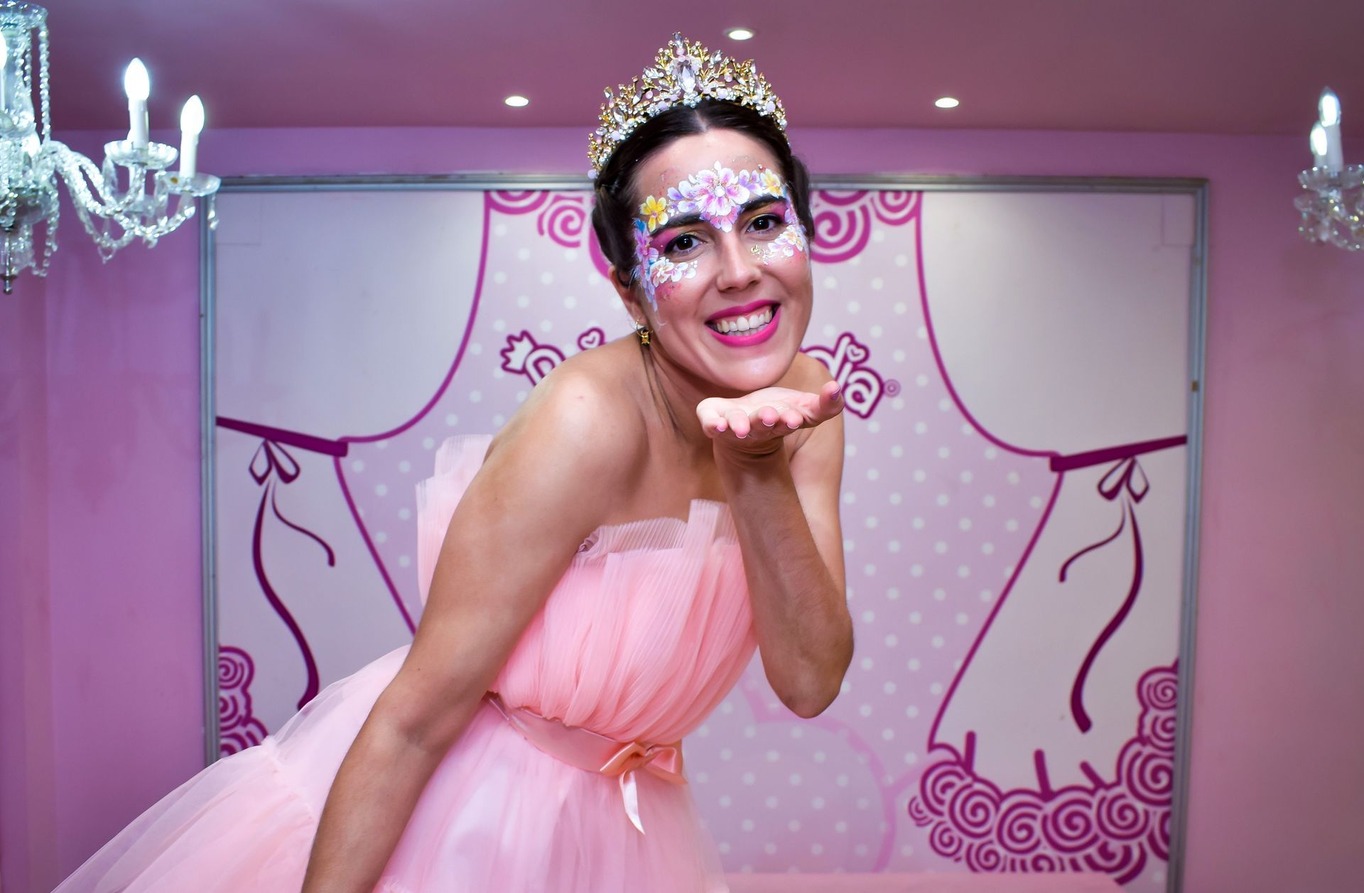 Una mujer con un vestido rosa y una tiara está lanzando un beso.