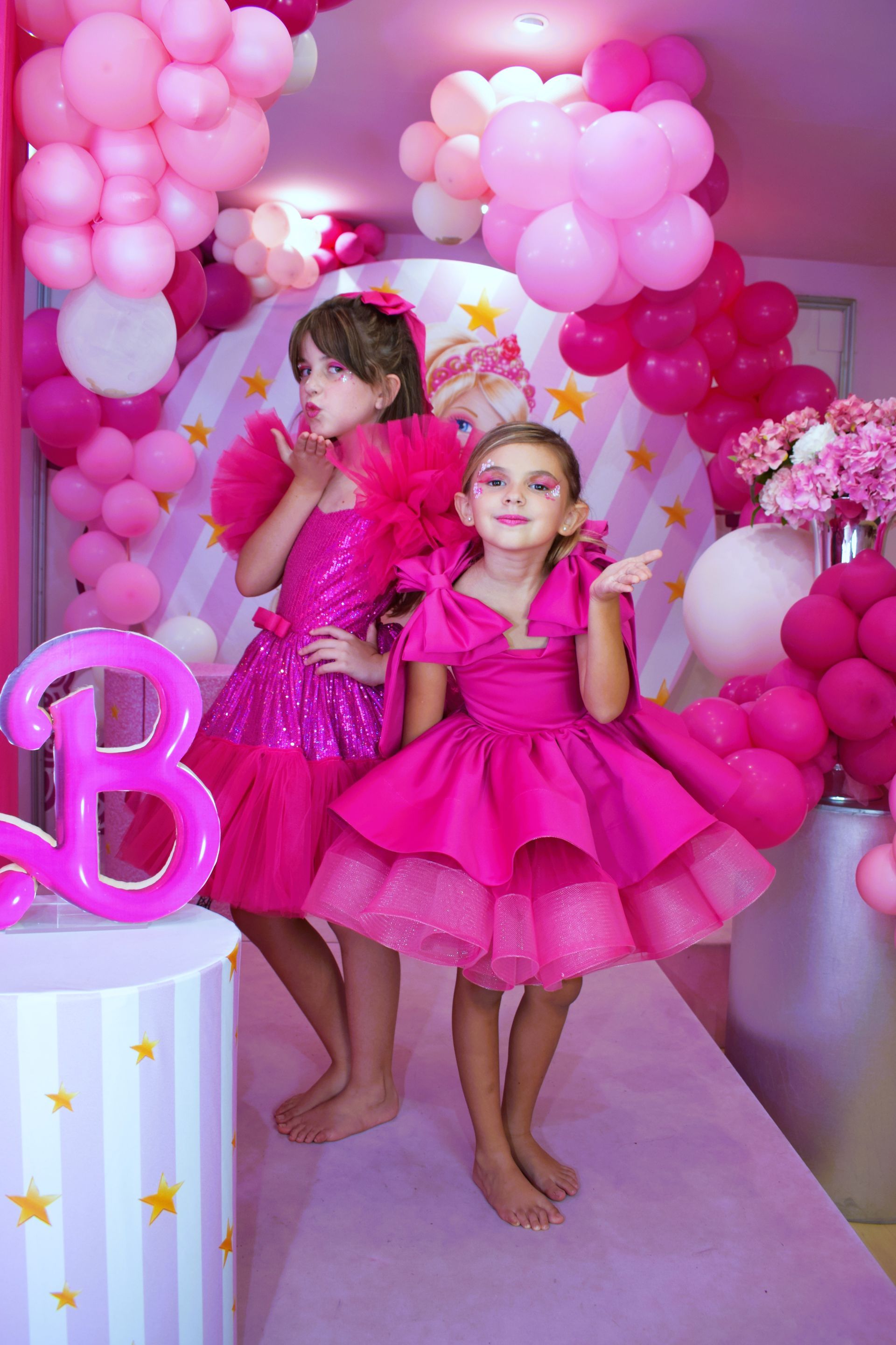 Dos niñas con vestidos rosas están paradas una al lado de la otra en una habitación decorada con globos rosas.
