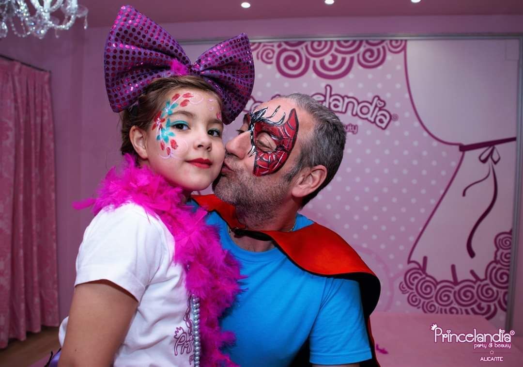 Un hombre y una niña posan para una fotografía. La niña lleva un lazo morado y una boa de plumas.