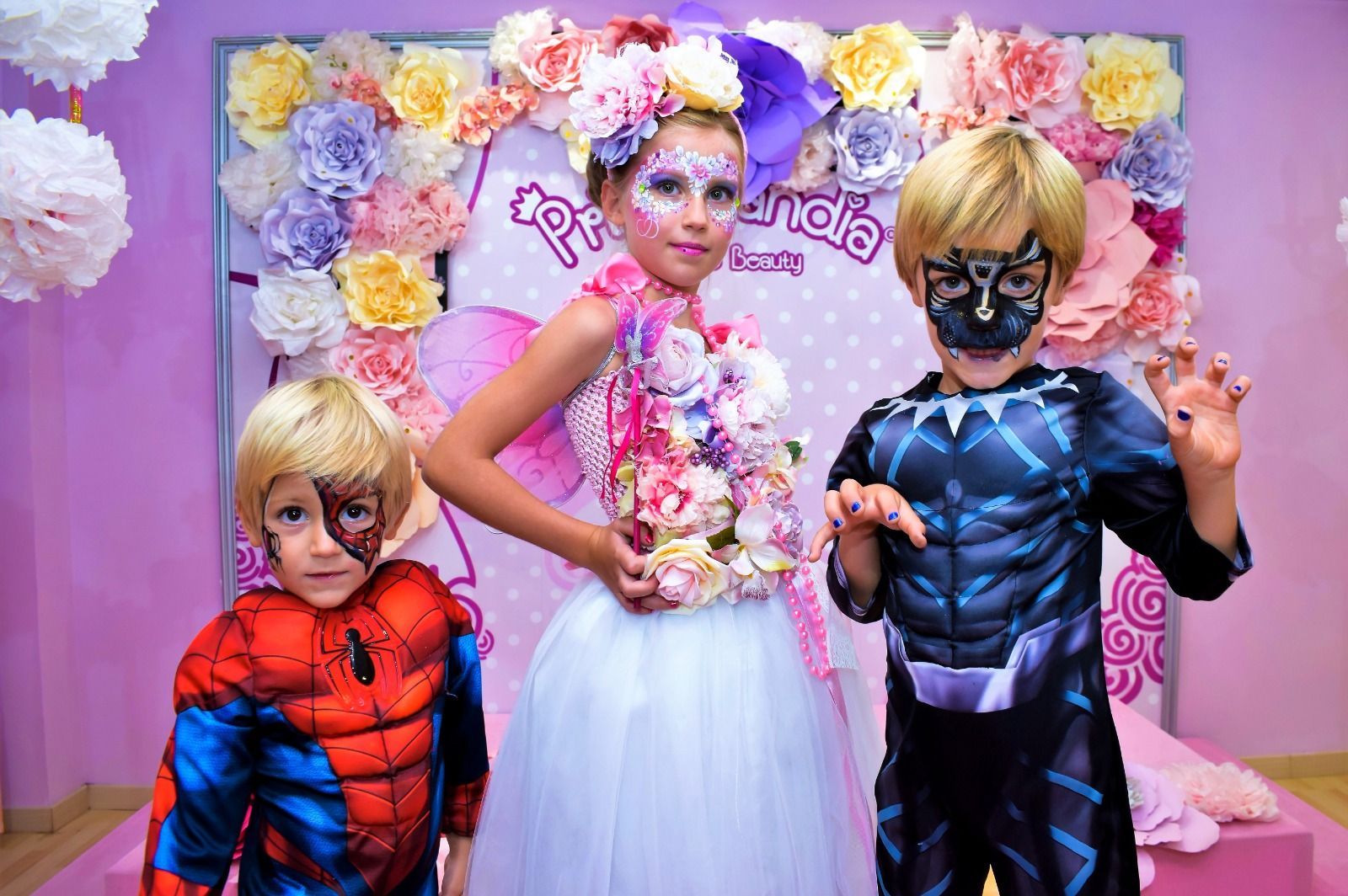 Una niña con flores pintadas en la cara está de pie junto a dos niños disfrazados.